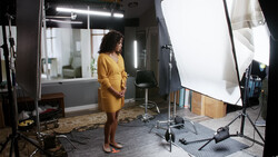 Woman in yellow dress standing in professional photo studio with softbox lighting and reflector setup.