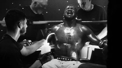 Boxer in ring receiving corner support between rounds in dramatic black and white photography.