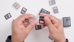 Hands holding SD memory cards with additional cards scattered on white surface.
