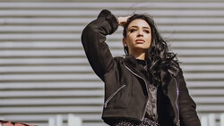 Woman in black jacket looking upward against corrugated metal backdrop.