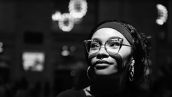 Person wearing glasses and headband looking upward in black and white portrait with bokeh lights in background.