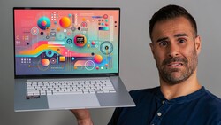 Man in dark blue shirt holding laptop displaying colorful abstract geometric design with circles and gradients.