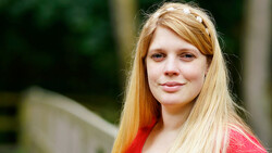 Young woman with long reddish-blonde hair looking directly at camera with neutral expression.