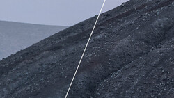 A white rope or cable cutting diagonally across dark, rocky slopes under overcast sky.