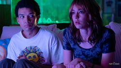 Two people sitting on a couch illuminated by green neon lighting from behind.