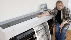 Photographer demonstrating a large-format inkjet printer with a tree branch print output.