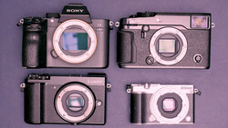 Four compact digital cameras arranged on a purple background, displaying various form factors and designs.