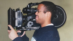 Cinematographer operating a 35mm film camera on his shoulder in profile.