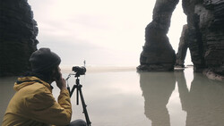 Photographer in yellow jacket using tripod to capture dramatic rock formations reflected in still water.