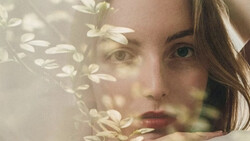 Woman's face partially obscured by delicate white flowers in soft, overexposed lighting.