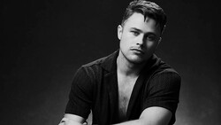 Black and white portrait of a man in an open textured shirt against a dark background.