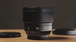 A 10mm prime lens with ribbed rubber grip and metal barrel displayed on wooden surface with soft studio lighting.