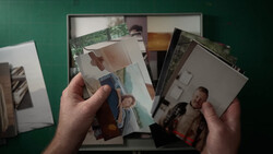 Hands holding scattered printed photographs against a green background with more prints visible below.