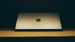Gold MacBook Pro closed on wooden surface against dark background with dramatic side lighting.
