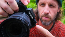 Photographer holding a mirrorless camera with telephoto lens attached, demonstrating proper grip and handling technique outdoors.