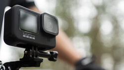 GoPro Hero 11 action camera mounted on a tripod bracket, shown in sharp focus against a blurred outdoor background.