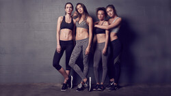 Four women in athletic wear posed against a textured gray wall.
