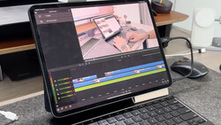 Screenshot of video editing software with timeline showing color-coded clips and preview of workspace setup on tablet screen.