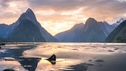 Dramatic fjord landscape with steep mountain peaks reflected in still water at golden hour.