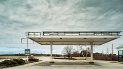 Abandoned gas station canopy with weathered concrete structure under overcast sky.