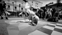 Breakdancer performing a headstand on a checkered street surface during a public performance.