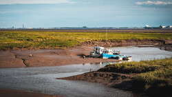 Fishing boat stranded on mudflats beside a shallow tidal channel during low tide.