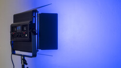Professional LED panel light mounted on stand with blue gel filter and control panel visible.