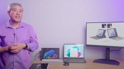 Man in purple shirt presenting laptop and monitor displays during a tech presentation.