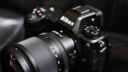 Nikon DSLR camera with attached zoom lens on dark background with secondary camera blurred in background.