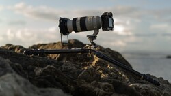 Professional telephoto lens mounted on tripod head positioned on rocky coastal outcrop.