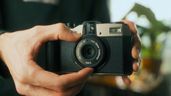 Hands holding a vintage rangefinder camera with textured black body and chrome accents.