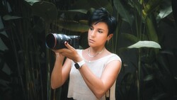 Photographer with telephoto lens among lush green foliage, composing a shot.