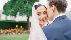 Bride in white veil smiling at groom during outdoor garden wedding ceremony.