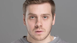 Portrait of a man with short brown hair against a neutral gray background.