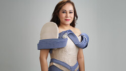 Woman in cream-colored off-shoulder dress with blue striped fabric draped around shoulders against neutral background.