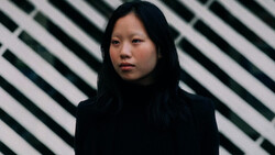 Portrait of a person with long dark hair against a striped geometric background.