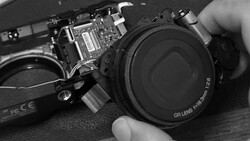 Disassembled compact camera showing internal circuitry and detached lens with GR branding.