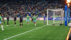 Professional soccer match at a large stadium with players in dark and green jerseys during evening play.