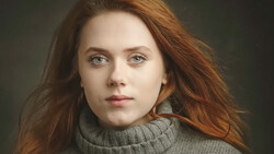 Woman with long reddish-brown hair wearing a gray turtleneck against a dark green background.