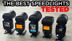 Five camera speedlights arranged in a row on a concrete surface for comparison testing.