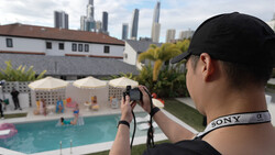 Photographer holding mirrorless camera with Sony strap, shooting poolside scene with city skyline beyond.