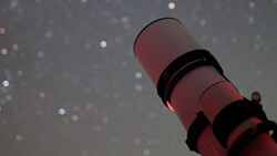 Red and black striped lighthouse tower shot from below against a bokeh background with soft light orbs.