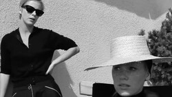 Two figures in sunglasses and dark clothing posed against a textured white wall in stark black and white photography.