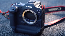 Canon EOS R3 mirrorless camera body without lens, displayed from front with open mount and red camera strap visible.