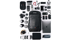 Flat lay of professional photography and videography equipment including camera body, lenses, backpack, laptop, batteries, and audio gear.