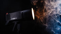 AD600Pro studio flash with warm and cool-colored smoke effects swirling around its illuminated head against black background.