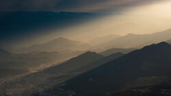 Layered mountain ranges receding into golden haze with silhouetted peaks in foreground and valley settlement visible below.