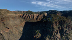 Deep canyon with layered rock formations and sparse vegetation under blue sky.