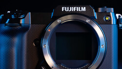 Fujifilm mirrorless camera body with lens mount exposed, front view against dark background with blue lighting.