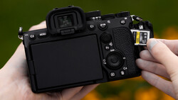 Mirrorless camera held in hands, showing rear LCD screen and control layout with various buttons and dials.